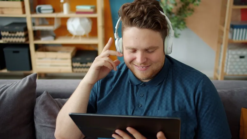 Man wearing wireless Bluetooth headphones while watching a video on a tablet at home