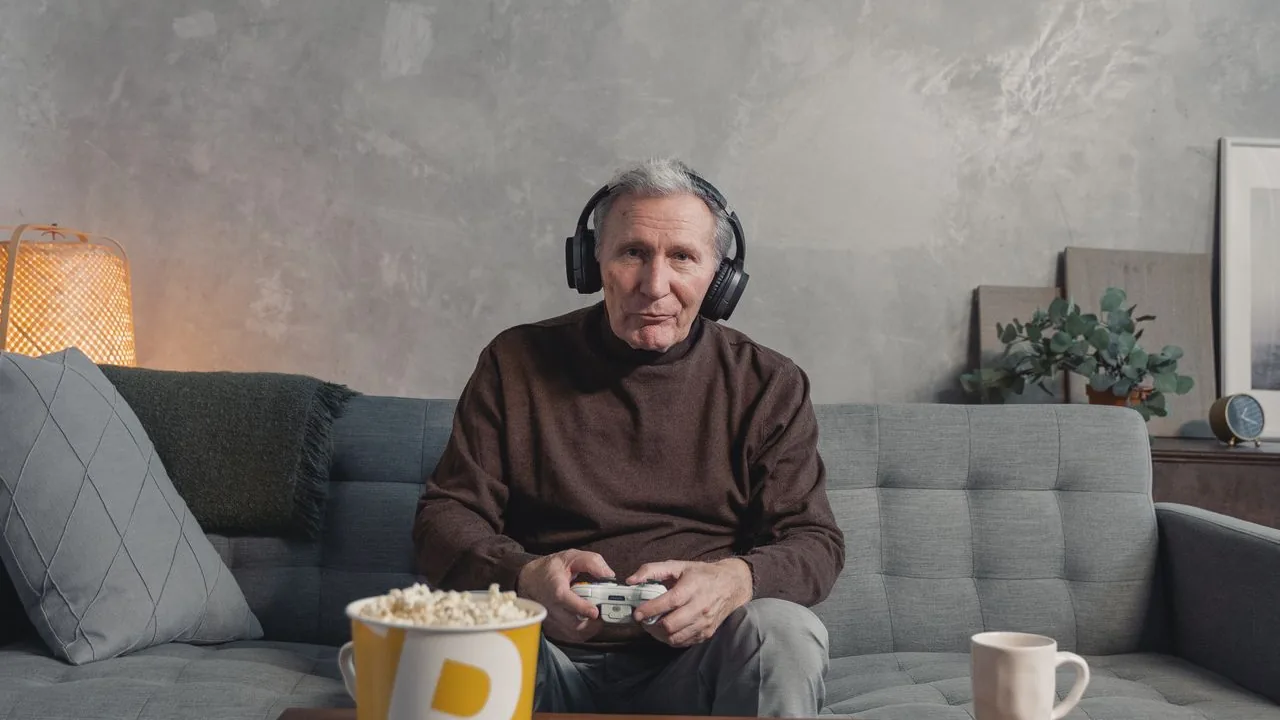 ソファでワイヤレスのBluetoothヘッドホンを着けてゲームコントローラーを握る男性