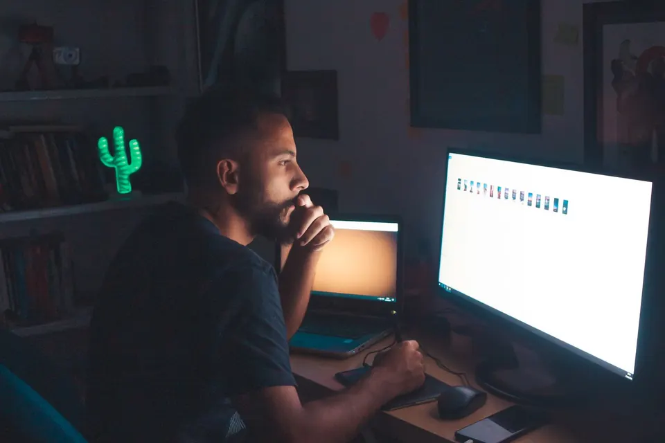 Hombre trabajando en una computadora en una habitación oscura iluminada sobre todo por el brillo del monitor