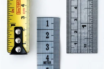 Yellow tape measure, fabric sewing tape and steel ruler lying side by side on a white desk