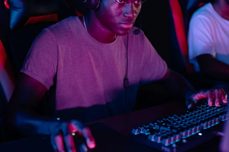 Pemain fokus memakai headset di meja esports gelap dengan satu tangan di mouse dan satu di keyboard menyala