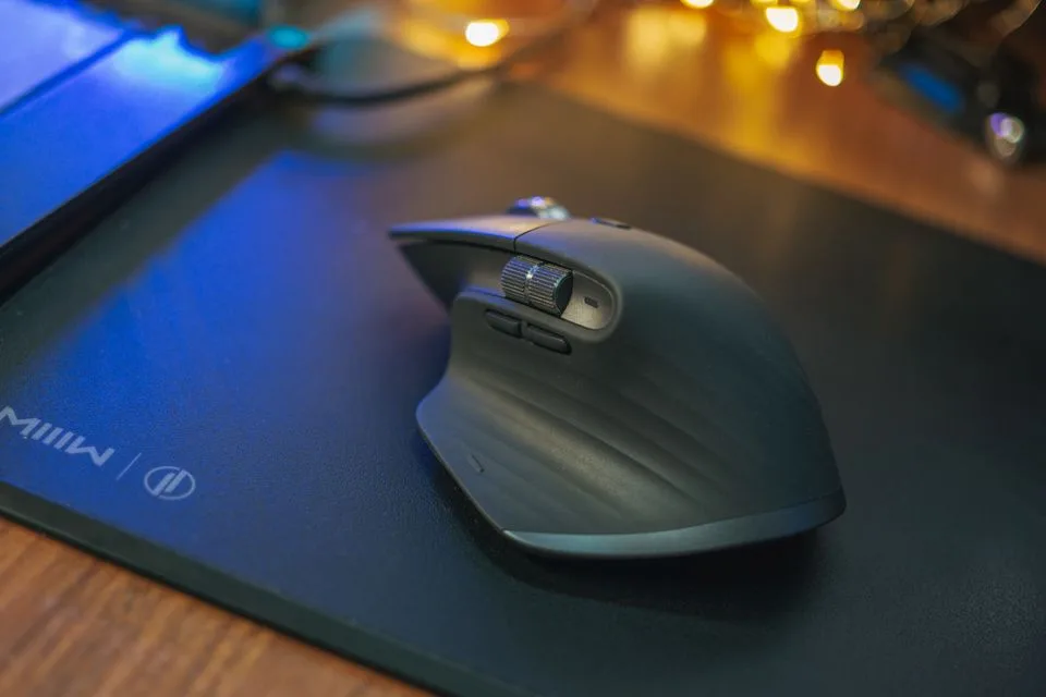Mouse nirkabel di atas mousepad kain hitam besar di meja kayu dengan lampu hangat di latar belakang