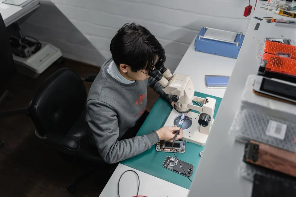 Repair technician working on a disassembled smartphone under a microscope at a workshop bench