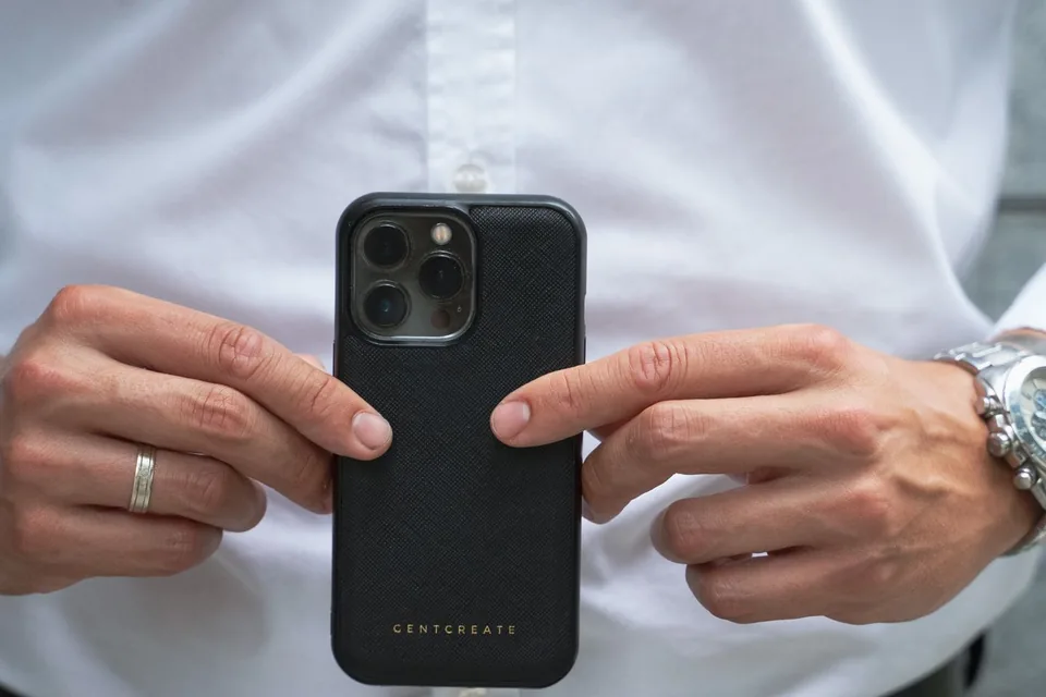Hands holding a smartphone in a thick black protective case while pointing at the back of the case