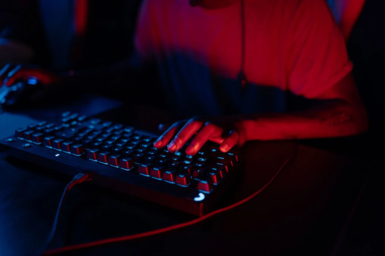 Руки печатают на игровой RGB-клавиатуре в красно-синей подсветке