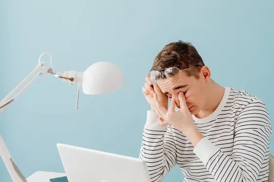 A tired person rubbing their eyes in front of a glowing laptop screen, a common sign of PWM flicker eye strain