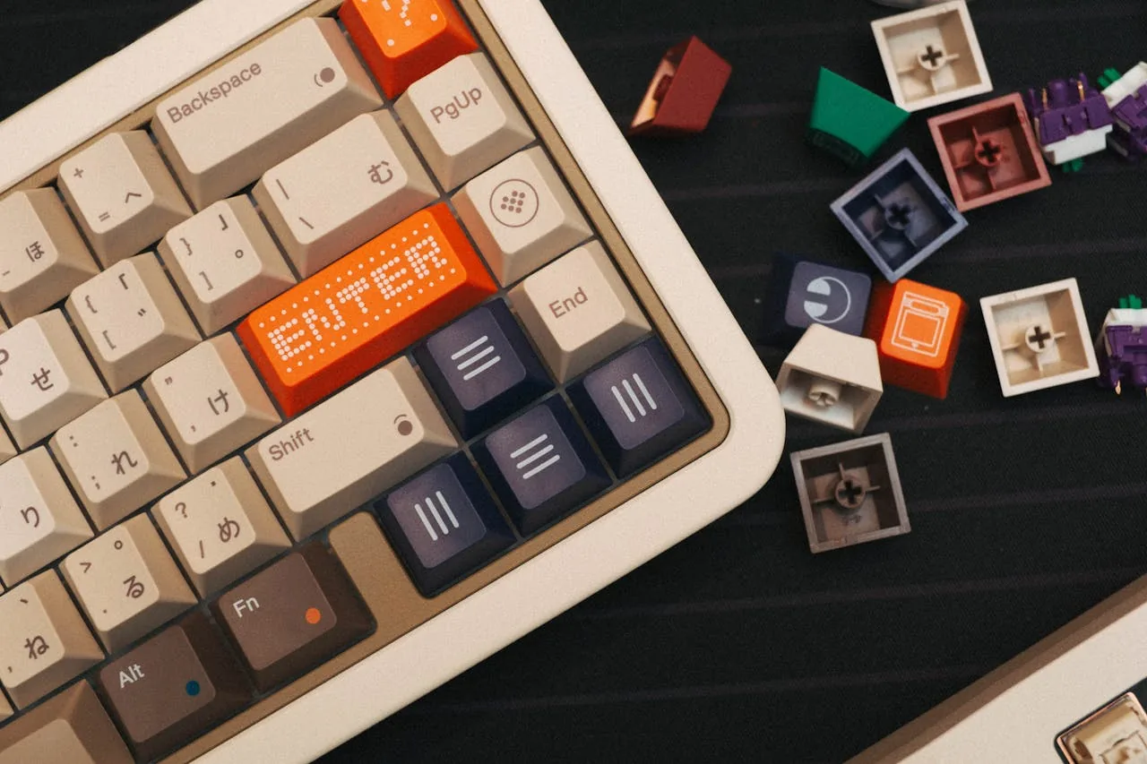 Top-down view of a beige mechanical keyboard with colourful custom keycaps and loose switches nearby — a build-in-progress typical of V4N4G0N owners assembling their boards
