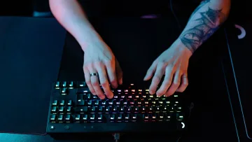 Hands of a gamer on a compact RGB mechanical keyboard on a dark desk mat