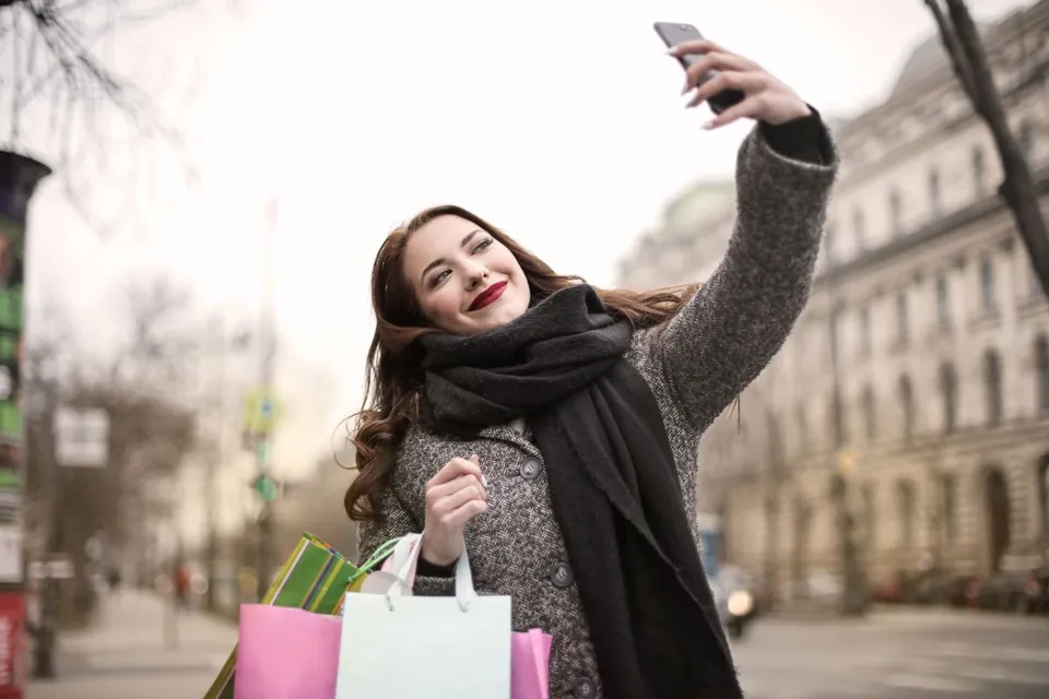 Wanita mengangkat smartphone dengan tangan terulur untuk selfie di jalanan kota