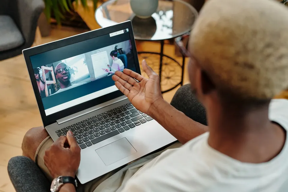 Pria mengangkat telapak tangan terbuka ke arah layar laptop saat video call di rumah
