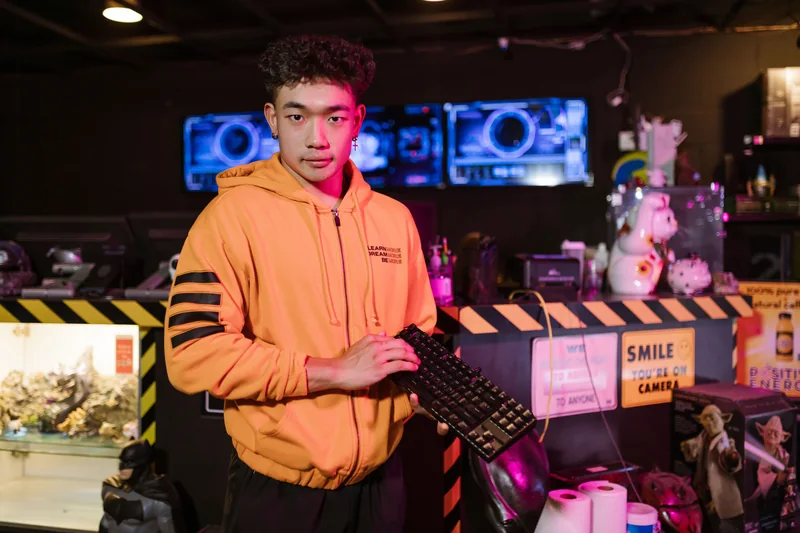 A person in an orange hoodie holding a mechanical keyboard in a gaming venue