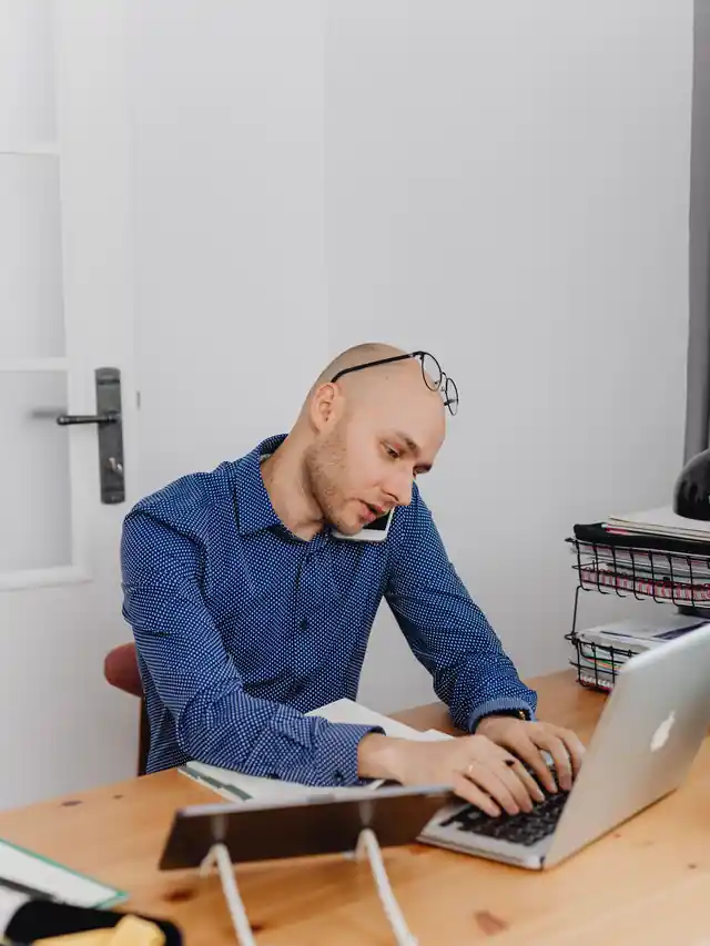 Illustrative stock photo of a man researching on a laptop while speaking on a phone