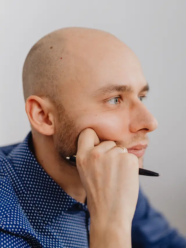 Illustrative stock photo of a thoughtful man holding a pen at an office desk