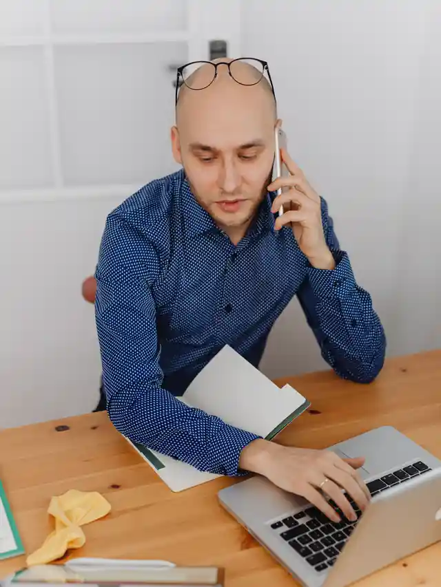 Illustrative stock photo of a man updating notes while working on a laptop and phone