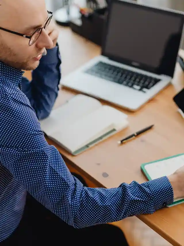 Illustrative stock photo of a man writing at a desk beside a laptop and tablet