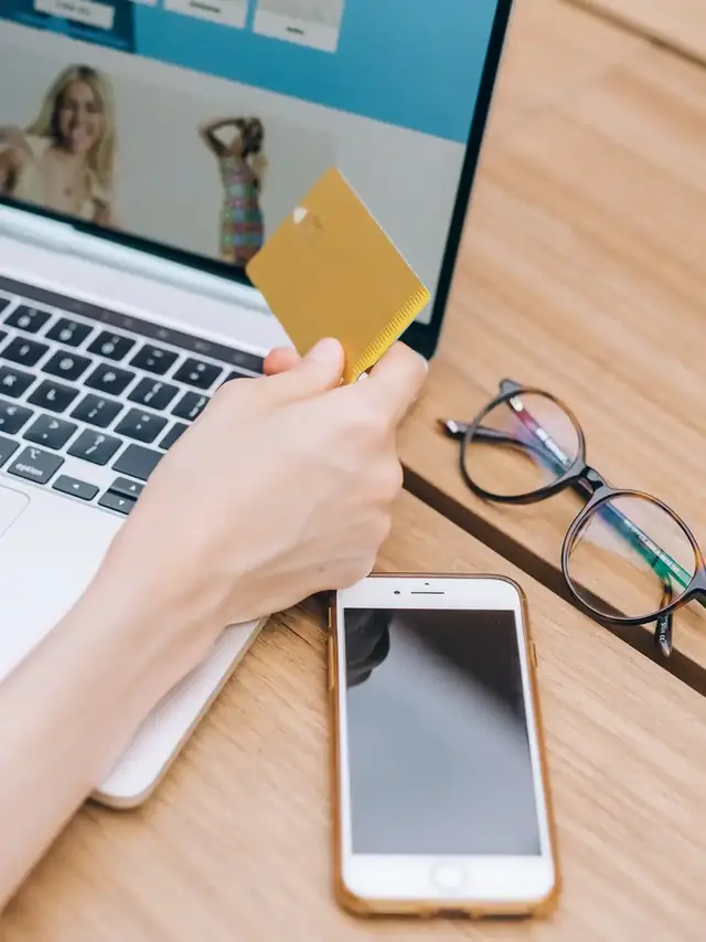 Hands using a payment card and laptop while researching an online product
