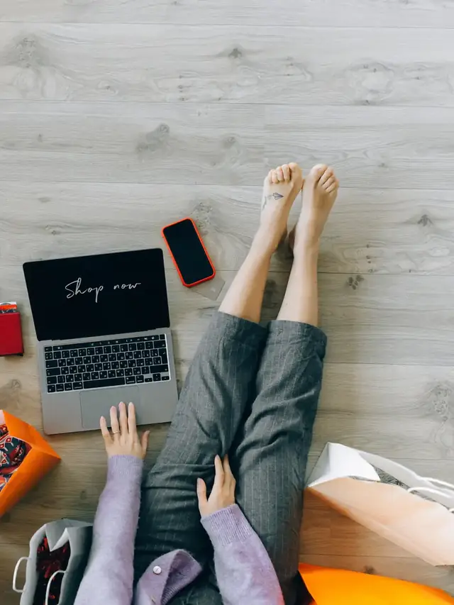 Person lying beside a laptop while comparing online prices