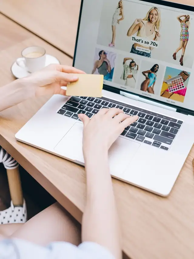 Person holding a payment card while reviewing a shopping page on a laptop