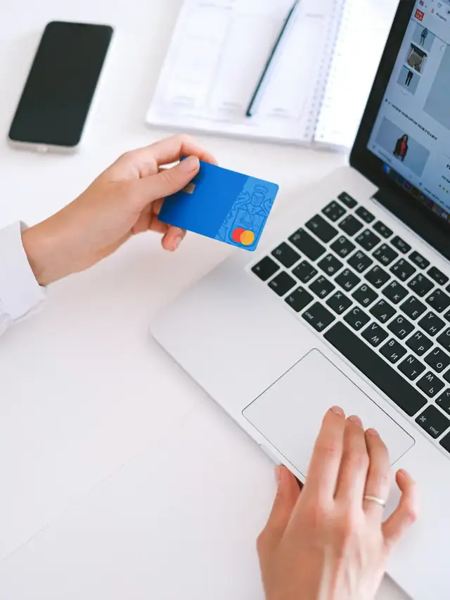 Hands comparing specifications with a payment card beside a laptop keyboard