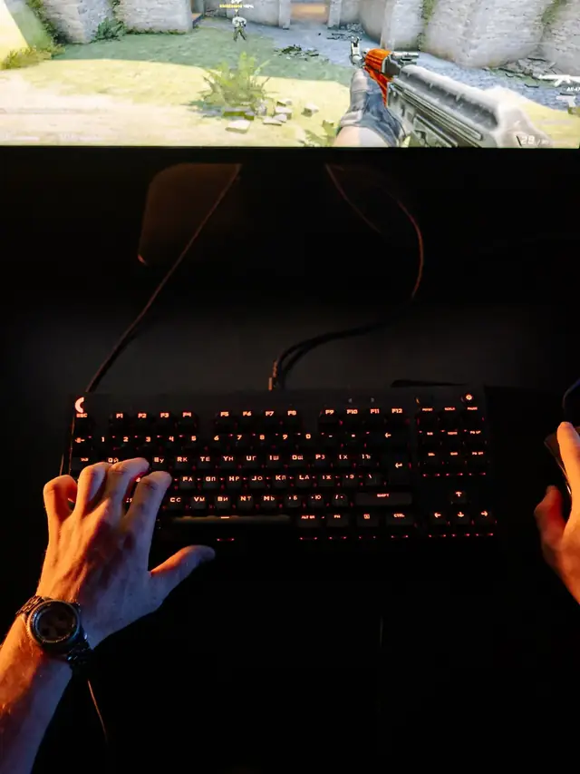 Hands controlling a keyboard and mouse with a shooter visible on the monitor; illustrative stock, not the example weapon
