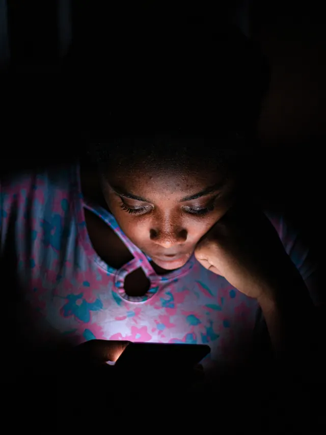Young woman absorbed in a smartphone screen in a dark room