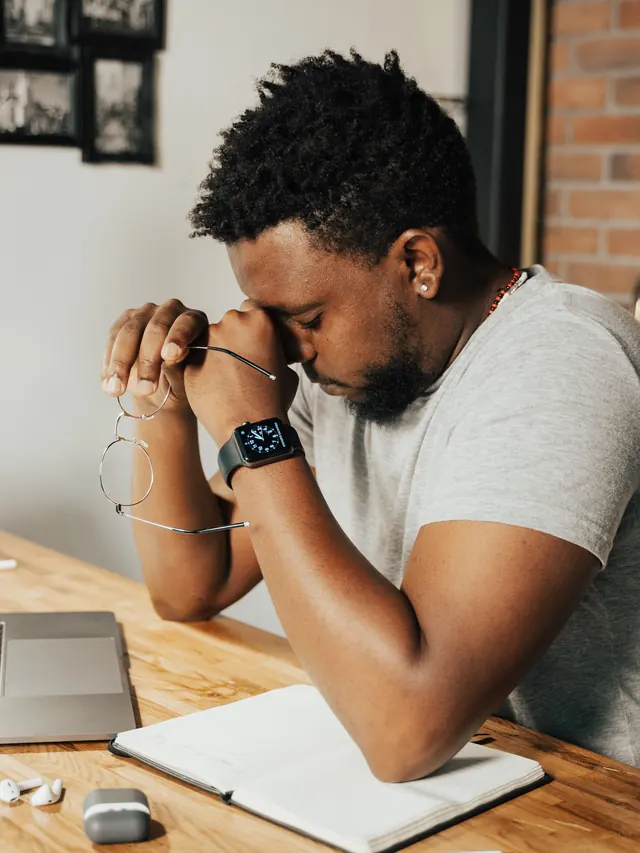 Exhausted man at a home desk rubbing his eyes beside a laptop