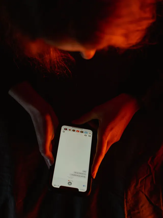 Person using a smartphone in dim, moody lighting