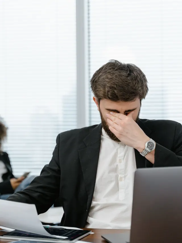 Businessman covering his eyes while working at a laptop