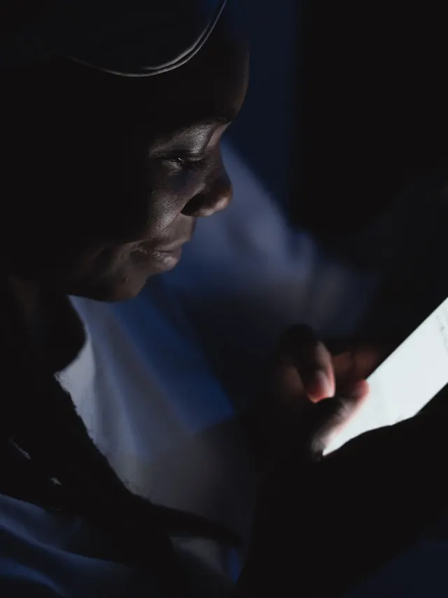 Woman reading her smartphone in a dark room, face lit by the screen