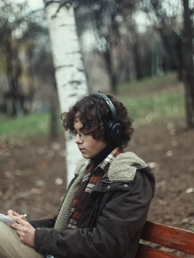Young man sitting on a park bench listening through headphones