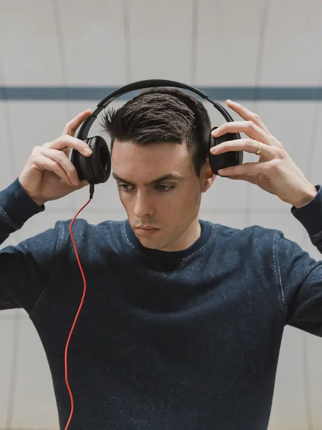 Young man adjusting a pair of black over-ear headphones indoors