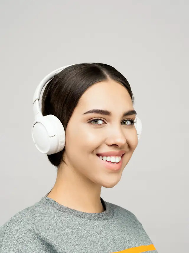 Smiling woman wearing white headphones while listening closely