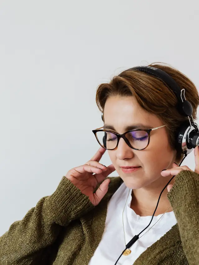 Woman wearing glasses and headphones listening to music indoors