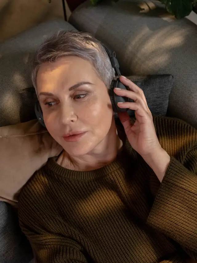 Senior woman with grey hair relaxing on a sofa wearing wireless headphones