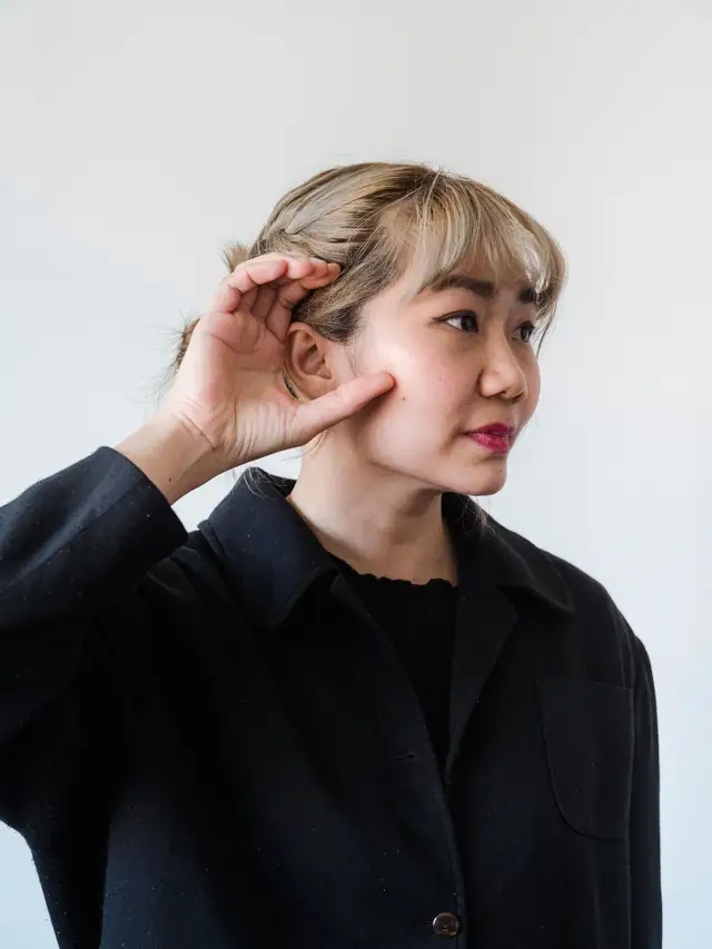 Woman cupping her hand to her ear in a listening gesture