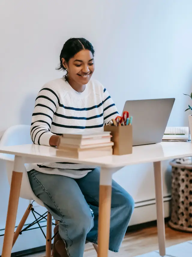 Woman working on a laptop behind a stack of books