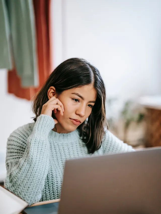 Woman resting her face on one hand while looking at a laptop
