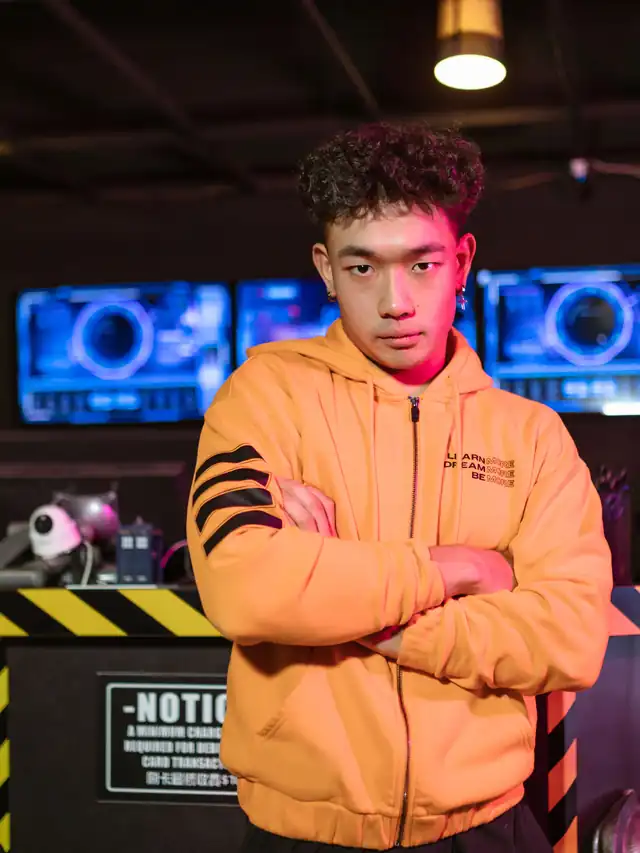 Young man in an orange hoodie standing with arms crossed, unconvinced