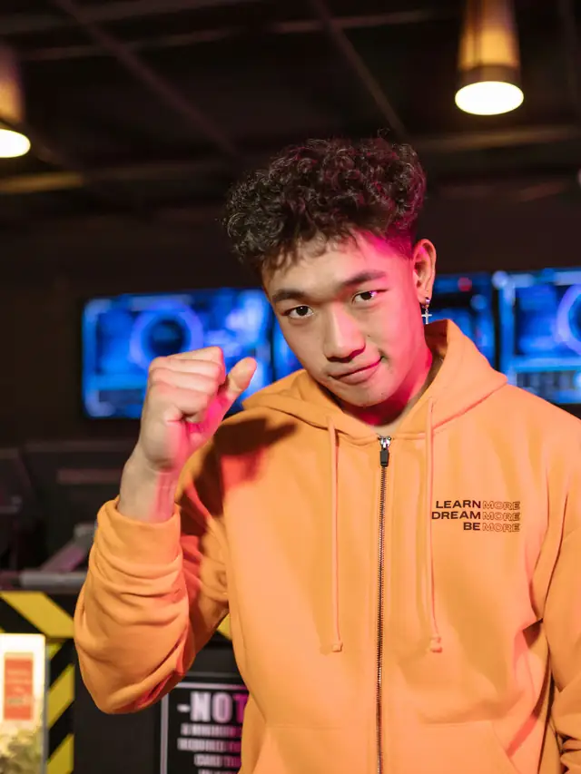 Young man in an orange hoodie smiling and raising a confident fist