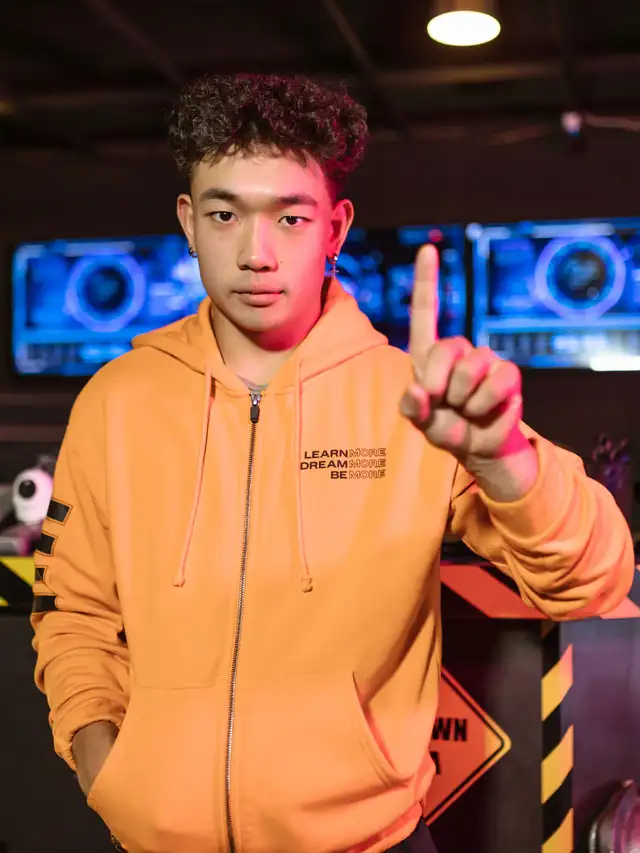 Young man in an orange hoodie holding a keyboard and raising one finger