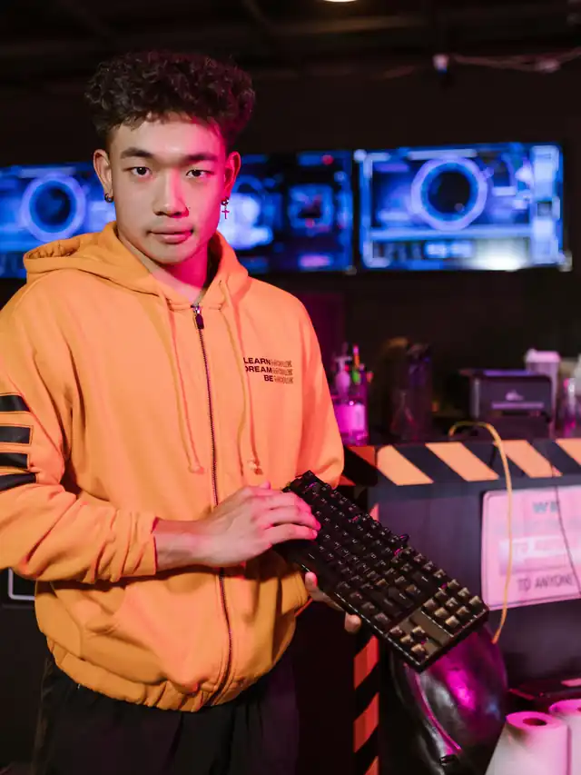 Young man in an orange hoodie examining a compact mechanical keyboard in a gaming cafe