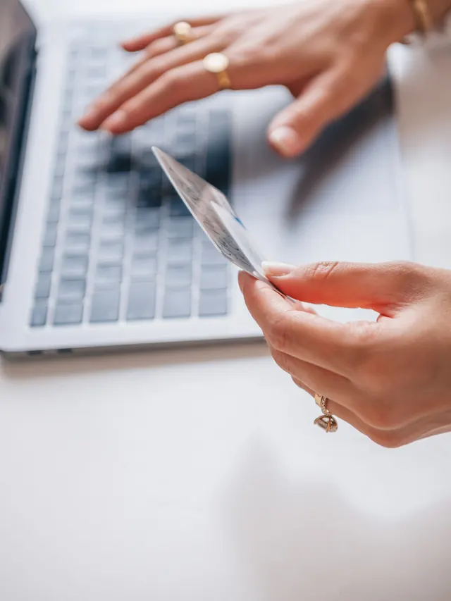 Woman holding a payment card while typing on a laptop