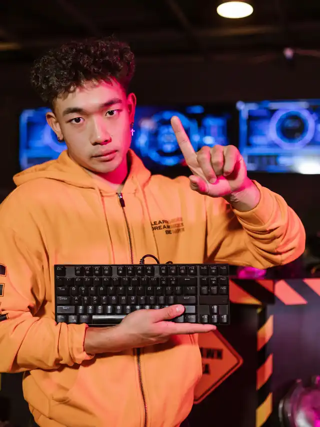 Young man in an orange hoodie holding a compact keyboard and pointing up