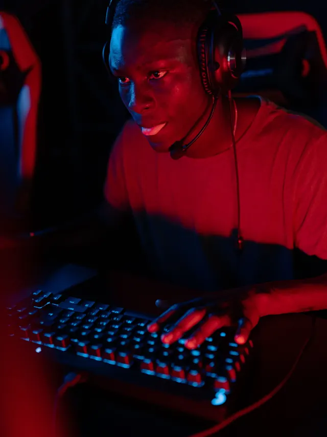 Headset-wearing gamer using a full-size keyboard under red and blue light
