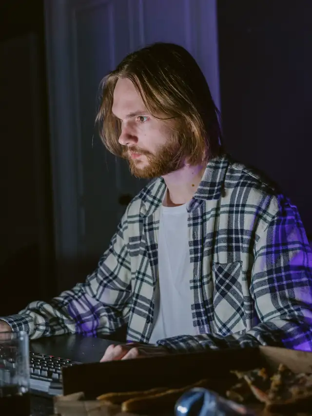 Focused gamer in a plaid shirt using a keyboard at a desk