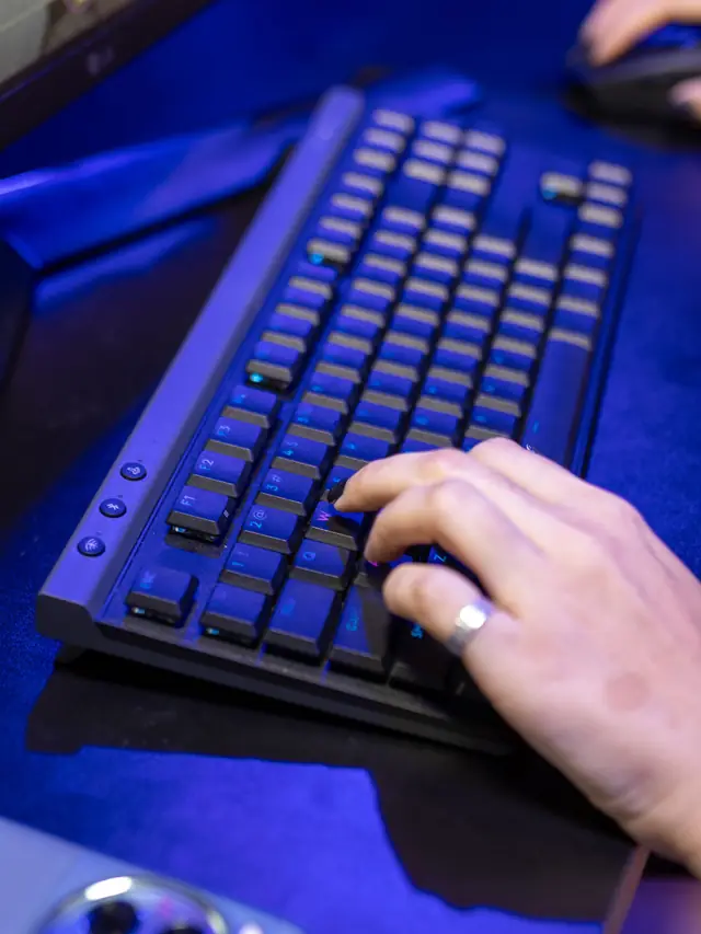 Hand pressing several keys on a blue-lit mechanical keyboard