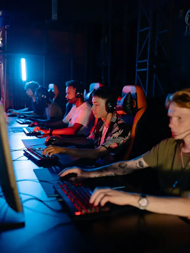 Row of esports players competing side by side at monitors in a blue-lit gaming arena
