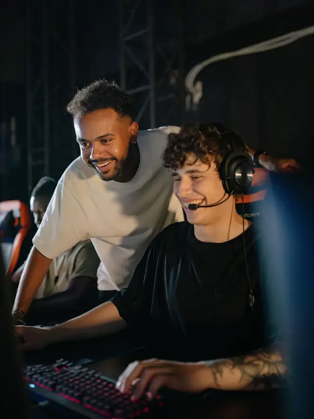 Two friends smiling while comparing options on a computer screen at a gaming event