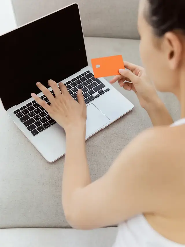 Person holding a card while typing on a laptop keyboard