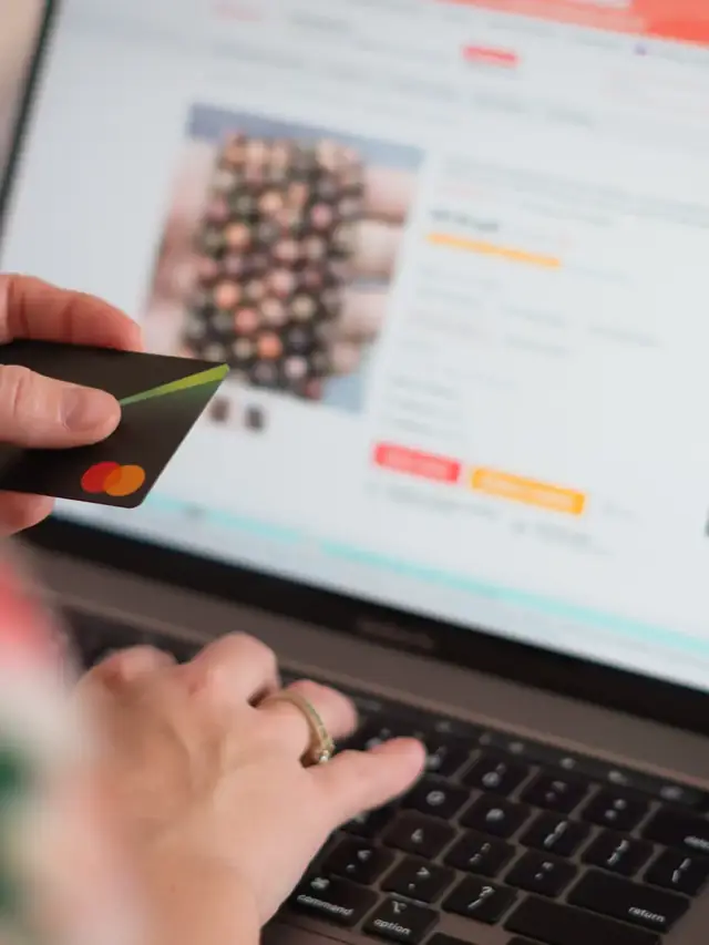 Hands using a payment card and laptop during product research